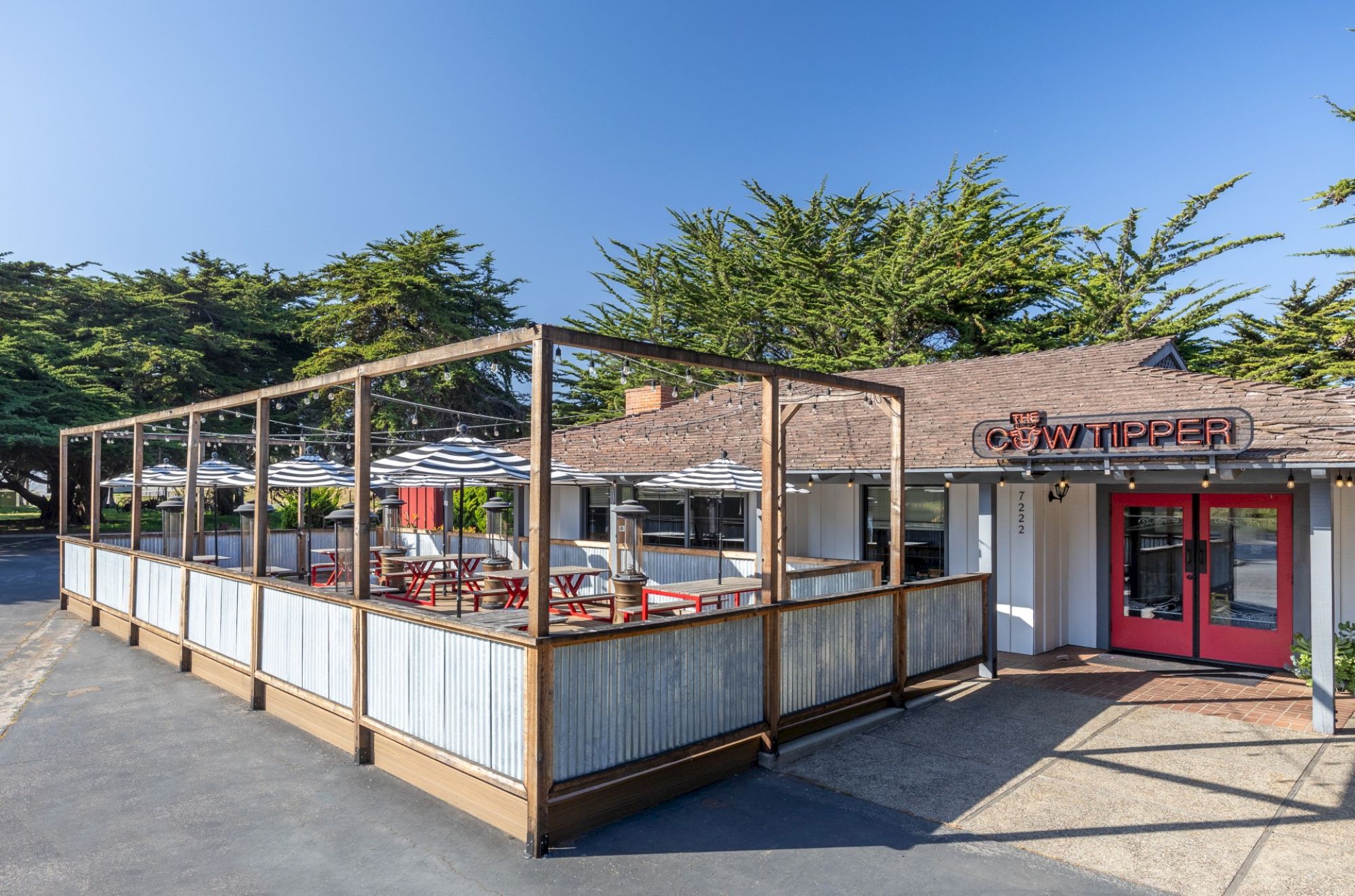 The image shows an outdoor dining area with tables, umbrellas, and a structure labeled "Tippets." The setting has clear skies and trees.