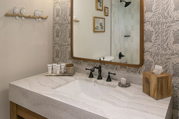 The image shows a bathroom with a marble countertop, black faucet, mirror, decorative wall, toiletries, tissue box, and small artworks on the wall.