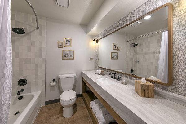 A modern bathroom with a large mirror, double sink, bathtub, toilet, and framed pictures on the wall creating a stylish ambiance.