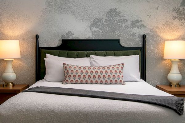 A neatly made bed with a decorative pillow, two pillows, and a throw blanket, flanked by two lit lamps on wooden nightstands.
