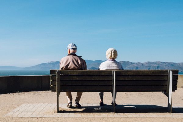 Two people sitting on a bench overlooking a vast landscape with mountains under a clear blue sky.