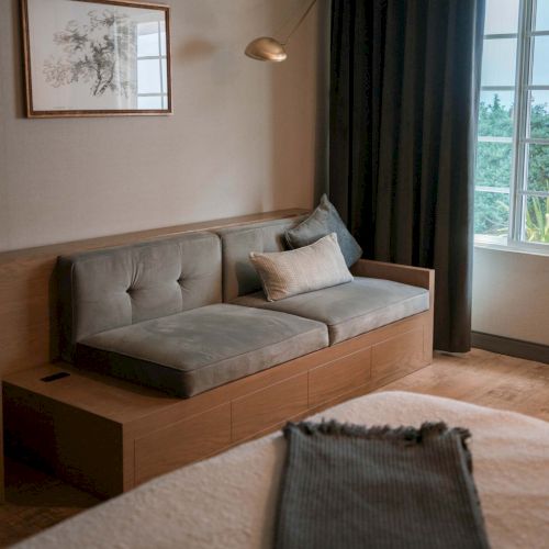 A cozy room with a gray couch, art on the wall, and a window draped with dark curtains enhances the relaxing atmosphere.