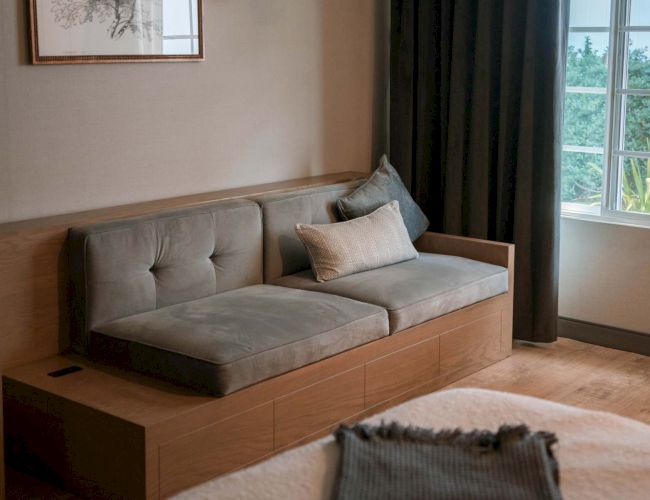 A cozy room with a gray couch, art on the wall, and a window draped with dark curtains enhances the relaxing atmosphere.