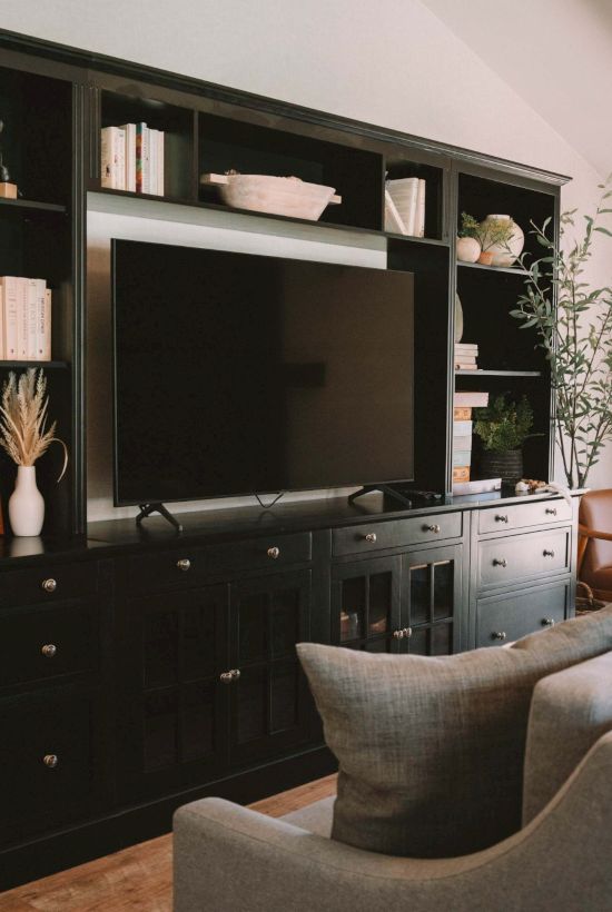 A living room with a dark wood entertainment center, books, decor, a large TV, sofa, chair, and window with a view outside.