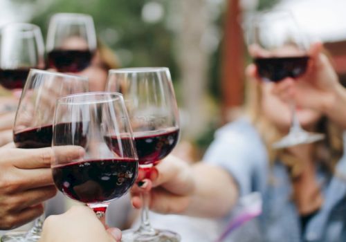 People raising glasses of red wine in a celebratory toast outdoors.
