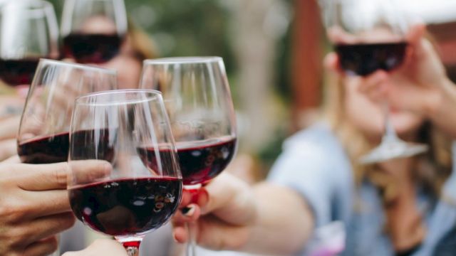People raising glasses of red wine in a celebratory toast outdoors.