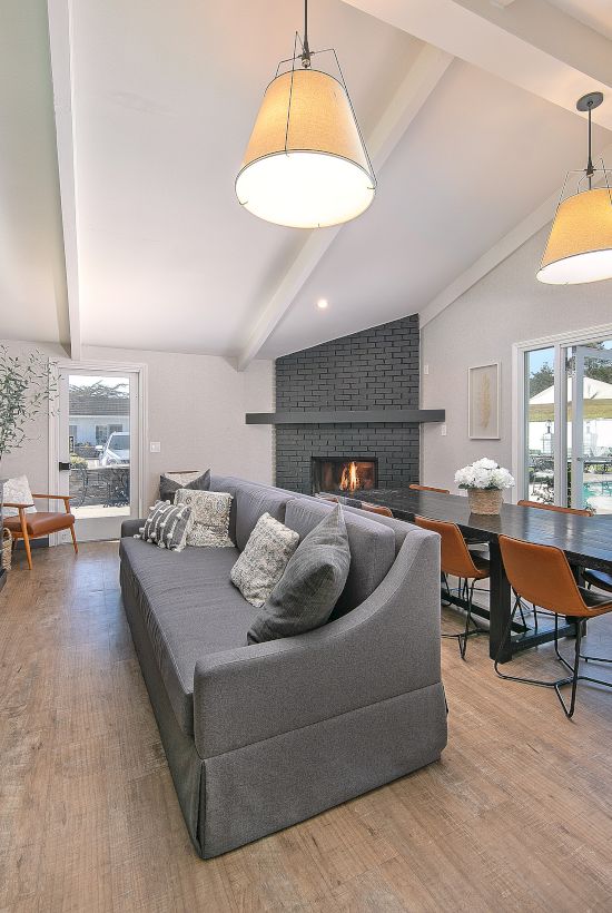 Cozy modern living room with a gray sofa, built-in dark media cabinet, wood floors, a fireplace, and large glass doors to an outdoor pool area, ending with a period.