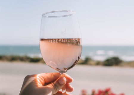 A person toasting with a glass of ros&eacute;, beach and sea in the background.
