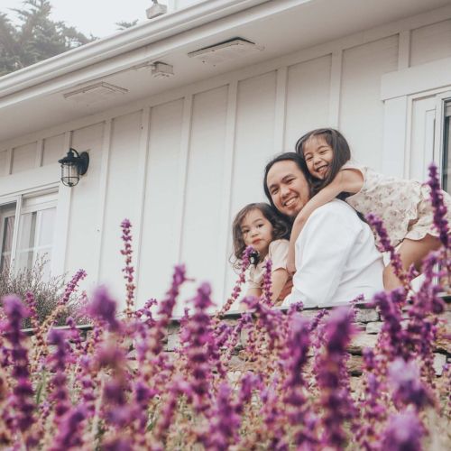 A couple with two children posing among blooming purple lavender in a garden near a white house.