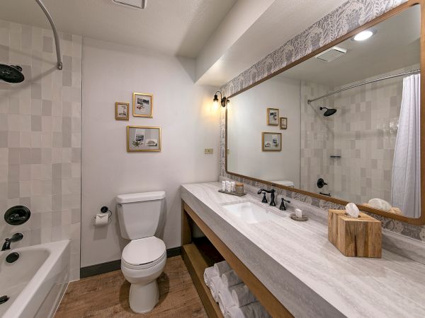 A modern bathroom with a bathtub/shower, toilet, dual sink vanity, oversized framed mirror, and light decor accents, tidy and bright.